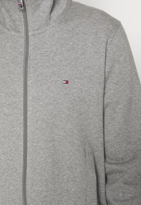 Gray zip-up sweatshirt made of soft fabric featuring a high collar, side pockets, and a small logo with red, white, and blue accents.