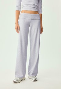 Hellgraue, weit geschnittene Sweatpants aus weichem Material. Sie verfügen über einen dicken Bund und eine lockere Passform, kombiniert mit silbernen Sportschuhen.