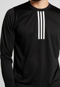 Camisa negra de manga larga hecha de tejido sintético, con tres rayas verticales blancas en la parte superior del pecho, textura suave.