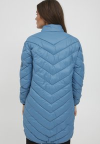 Ljusblå puffjacka med ett chevron-quiltat mönster, hög krage och elastiska ärmslut, med en överdimensionerad silhuett och mjuk textur.