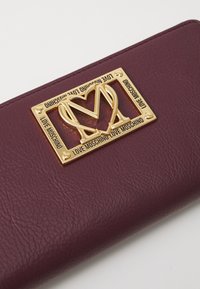 Burgundy faux leather wallet featuring a gold-tone love heart and “Love Moschino” logo plaque, rectangular shape, textured surface.