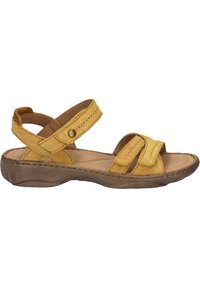 Sandale en suede jaune avec des sangles croisées et des sangles de cheville ajustables, dotée d'une semelle intérieure rembourrée et d'une semelle en caoutchouc brune contournée.