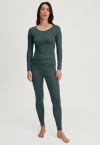 Haut ajusté à manches longues et leggings en vert foncé, fabriqués à partir d'un tissu doux et extensible avec une texture lisse et un col rond.