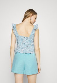 Modrý top s květinovým vzorem a peplum střihem, s volánkovými ramínky, v kombinaci se světle modrými lněnými šortkami, který má vykrojenou zadní část.