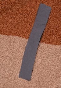 Grijze stofstrip geplaatst op een getextureerde, meerkleurige fleece achtergrond met tinten bruin en lichtbeige, met een zachte, pluizige textuur.