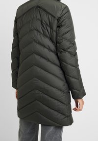 Mörkgrön puffjacka med chevron-quiltdesign, långa ärmar och en avslappnad passform. Slät, blank yta med hög krage.