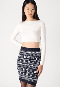 Un haut court à manches longues crème associé à une jupe crayon en tricot navy arborant des motifs de rennes et de flocons de neige blancs.