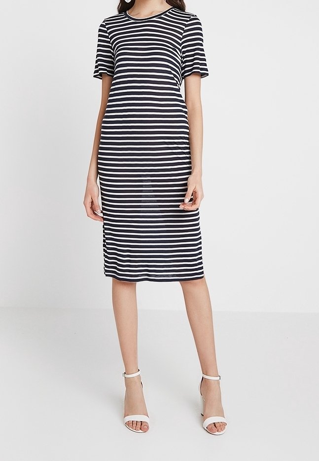 Robe rayée avec manches courtes, col rond et longueur au genou, en rayures bleu marine et blanc. Associée à des talons blancs.