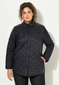 Chaqueta negra acolchada con cuello tipo solapa, cierre de botones y dos bolsillos en el pecho. Presenta un patrón texturizado y mangas largas.