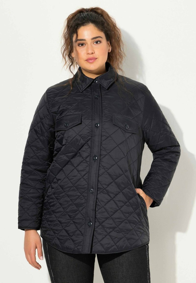 Chaqueta negra acolchada con cuello tipo solapa, cierre de botones y dos bolsillos en el pecho. Presenta un patrón texturizado y mangas largas.