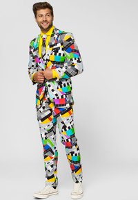 Colorful patterned suit in white, featuring geometric shapes in red, blue, green, yellow, and black. Paired with a bright yellow shirt and sneakers.