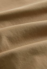 Kerge pruun kangas pehme tekstuuriga, millel on sile, kergelt sooneline pind ja peen sära, korraldatud õrnades voltides.