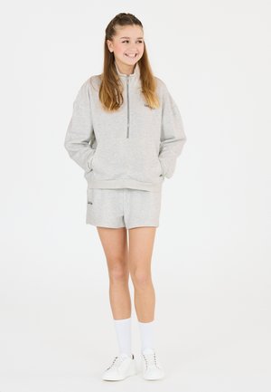 Grå fleecetröja med halvmidja och framfickor, kombinerad med matchande shorts. Vita sneakers och knästrumpor fulländar stilen.