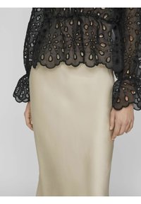 Svart broderad genomskinlig topp med blommig utskärning och scallop detaljer, i kombination med en slät beigt satin kjol. Toppen har puffärmar.