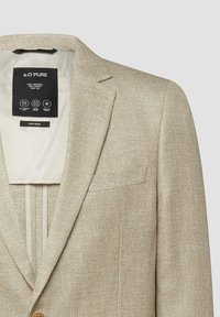 Blazer beige en mélange de lin avec un col à revers cranté, une poche poitrine et une doublure intérieure claire montrant une étiquette de marque noire sur le col.