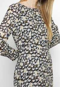 Vestido floral con base de un oscuro azul marino, con pequeñas flores blancas y beige. Mangas largas, cuello redondo y una cintura ceñida.