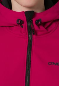 Różowa kurtka z kapturem, z czarnym wnętrzem, z pełnym zamkiem błyskawicznym i regulowanym troczkiem w kapturze. Posiada czarne logo na piersi.