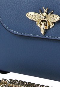 Sac bandoulière en similicuir bleu avec un fermoir doré en forme d'abeille et une bandoulière chaîne décorative à motif ondulé.