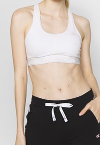 Bílá sportovní podprsenka s kulatým výstřihem, nastavitelnými ramínky a elastickým páskem s logem "Adidas".