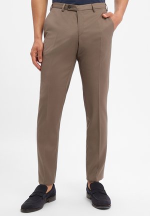 Mann trägt braune Slim-Fit-Anzughose mit Seitentaschen und schwarze Loafer vor weißem Hintergrund.