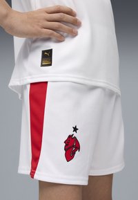 Weiße Sportshorts mit roten Seitenstreifen, ausgestattet mit einem schwarzen und roten Drachenlogo sowie einem goldenen Puma-Echtheitslabel.