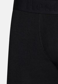 Schwarze Baumwollboxershorts mit einer weichen Textur, ausgestattet mit einem breiten Bund, der das Wort "Rest." eingeprägt hat, und einer gestickten Naht auf der Vorderseite.