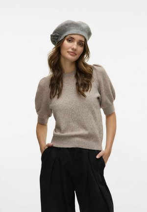 Gorro de lana gris con un adorno de flor lateral, combinado con un suéter de punto de manga corta beige y pantalones negros de raya. Textura suave.