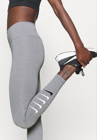 Szare legginsy sportowe z elastycznego materiału, o gładkiej teksturze, z czarnym logo Nike i białymi detalami na boku.