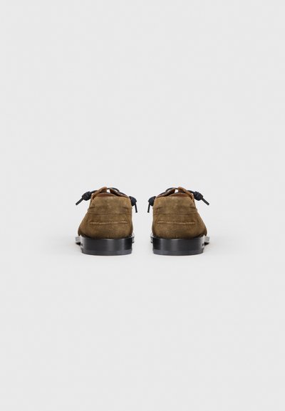 Chaussures en daim marron à profil bas, avec une semelle noire lisse et des lacets foncés. La vue arrière met en évidence les détails de la couture et la forme arrondie.