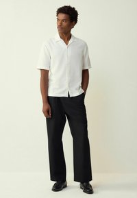 Short-sleeve white button-up shirt with a textured pattern, paired with relaxed black trousers and black shoes. Simple, modern design.