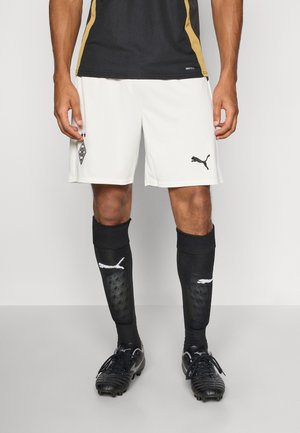 Hvide fodboldshorts med et sort Puma-logo og mærke, parret med sorte sokker med hvide accenter og strukturerede paneler. Sorte fodboldstøvler.