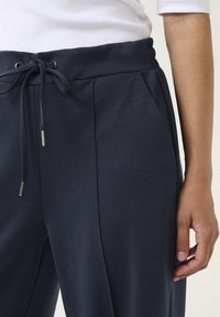 Navy blauwe joggingbroeken van gestructureerde stof, met een elastische tailleband met trekkoord en subtiele voorplooien.