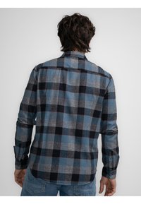 Camisa de franela para hombre con un patrón de cuadros en azul, negro y gris. Mangas largas, puños abotonados y un dobladillo recto para un ajuste relajado.