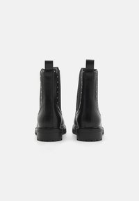 Bottines noires en cuir avec des panneaux élastiques sur les côtés et des clous en argent le long des coutures, dotées d'une semelle en caoutchouc robuste et de languettes de tirage.