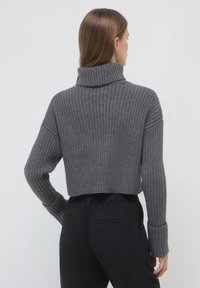 Maglione grigio a coste, accorciato, con colletto alto e maniche lunghe, caratterizzato da ampi polsini. Texture morbida visibile nel motivo a maglia.