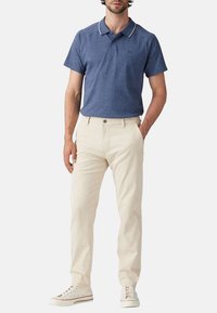 Polo shirt bleu foncé avec bordure de col blanche, pantalon en lin beige et baskets blanches. Design simple et classique avec une coupe décontractée.