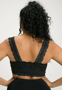 Svart spetsbralette med blommönster, scallopkanter och breda spetsremmar. Designen erbjuder en rygglös silhuett.