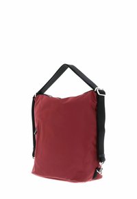 Sac en nylon rouge avec une bandoulière noire réglable ; forme carrée ; dispose d'une poche zippée sur le côté ; texture lisse avec des accents matériels minimaux.