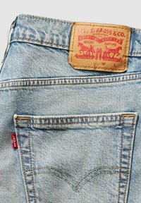 Jasnoniebieskie jeansy z denimu z skórzaną naszywką z czerwonymi napisami i wzorami, żółtym przeszyciem oraz małą czerwoną metką Levi's po bokach.