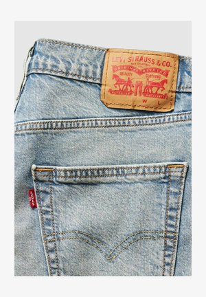 Jasnoniebieskie jeansy z denimu z skórzaną naszywką z czerwonymi napisami i wzorami, żółtym przeszyciem oraz małą czerwoną metką Levi's po bokach.