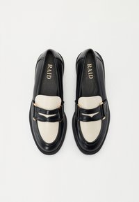 Svarte og kremfargede loafers med en blank finish, med en gullfarget spenne som aksent og et rundt tådesign. Flate såler.