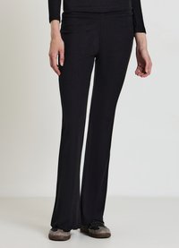 Schwarze Rippengamaschen mit ausgestelltem Saum, die eine schmal geschnittene Passform und eine weiche Textur aufweisen, kombiniert mit grauen Slippers.