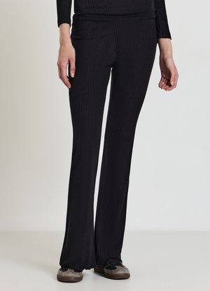 Schwarze Rippengamaschen mit ausgestelltem Saum, die eine schmal geschnittene Passform und eine weiche Textur aufweisen, kombiniert mit grauen Slippers.