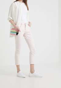 Jeans cortos de color rosa claro con un corte ajustado, combinados con una camiseta blanca y una camisa crema de botones. Zapatillas blancas completan el atuendo.
