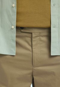 Groen en wit geruit overhemd over een mosterdkleurige trui, gecombineerd met lichtbruine rechte broek.