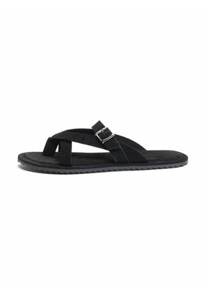 Sort flad sandal med krydsede ruskindsstropper og en sølvspænde på en rippet gummisål, vist fra siden på en hvid baggrund.