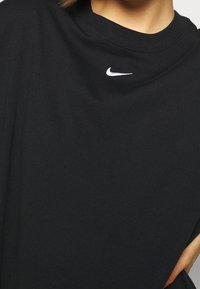 Svart bomull T-shirt med rund hals som har en liten vit Nike-logga på övre vänstra bröstet; tyget ser slätt och lätt ut.