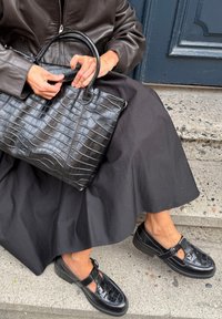 Black crocodile-patterned leather handbag with a structured shape, paired with black T-bar shoes featuring buckle detail and textured finish.