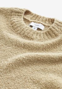 Beige, gewatteerde trui met een ribbel gebreide ronde hals. Etiket zichtbaar met het merk "NEXT" en maat "M". Zacht, pluizig stof.