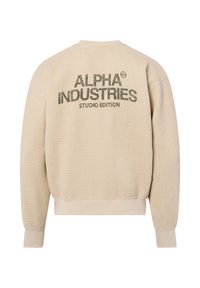 Beige gebreide sweatshirt met een gestructureerd patroon, met een grote print in donkergroen op de achterkant met de tekst "ALPHA INDUSTRIES STUDIO EDITION."